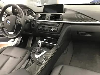 Car interior with the dashboard trim and centre console wrapped in Carbon Fiber Black, a BMW roundel on the steering wheel