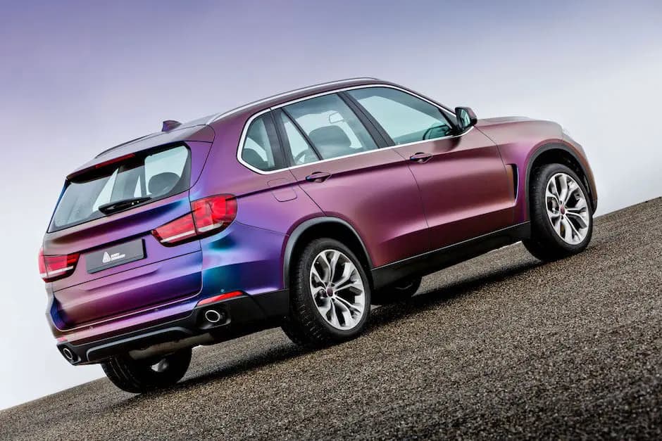 Rear three-quarter view of a full-size SUV wrapped in ColorFlow Rushing Riptide, purple over the doors and rear quarter turning cyan across the tailgate and bumper, with an Avery Dennison plate in the licence plate recess