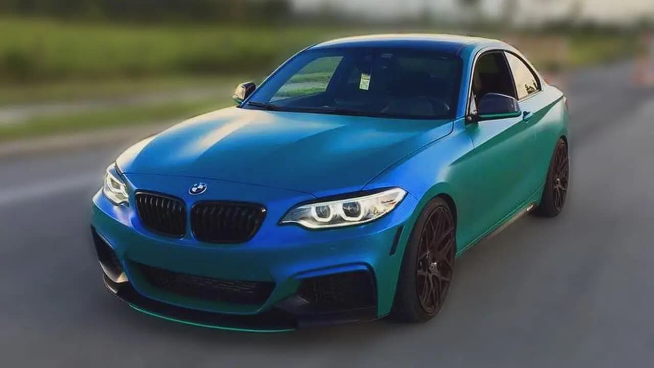 BMW coupe on a road, wrapped in Satin Flip Caribbean Shimmer, blue across the hood and front fender shifting to green along the doors and rear quarter, on bronze wheels