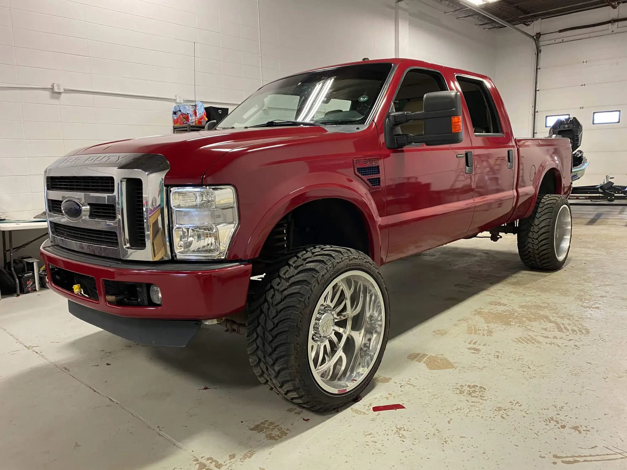 Lifted Ford F-350 Super Duty crew cab pickup in a shop bay, wrapped in Gloss Cinder Spark Red