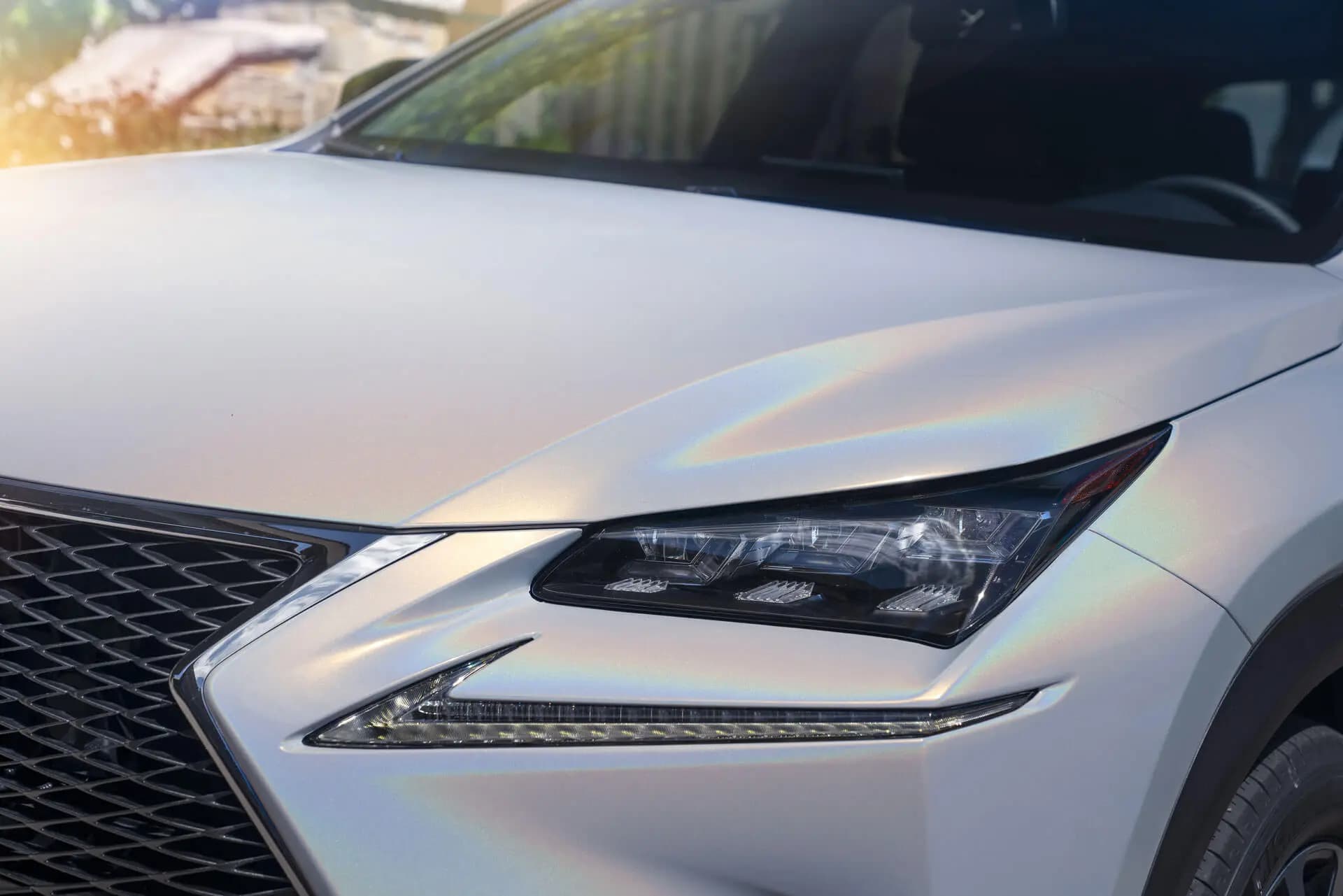 Close-up of a Lexus SUV front corner, hood and headlight, wrapped in pearl white Gloss Flip Ghost Pearl with a faint rainbow sheen across the panel