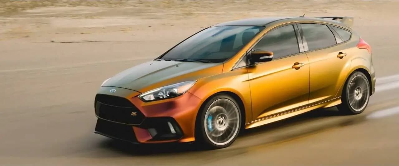 Ford Focus RS hatchback wrapped in Satin Flip Volcanic Flare, moving on a sandy road, the colour reading gold along the doors and copper over the front bumper